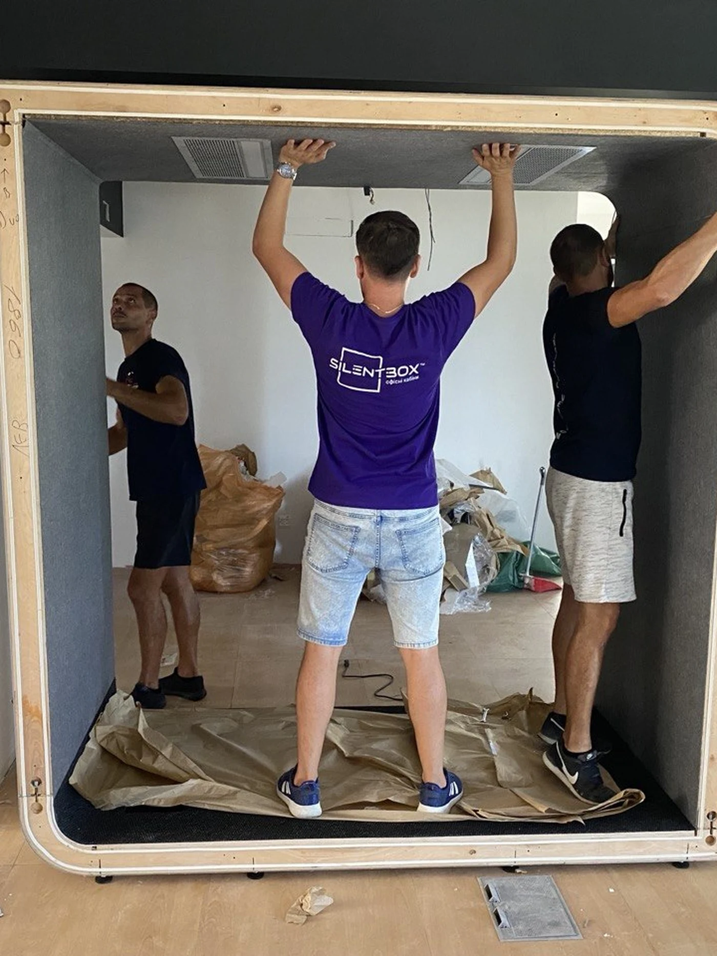 Three Silentbox installers fitting the ceiling panel of an assembled booth frame on-site