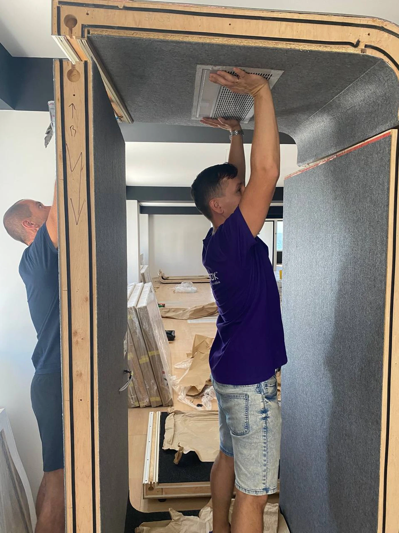 An installer fitting the ventilation grille of a Silentbox booth ceiling panel from inside, on-site